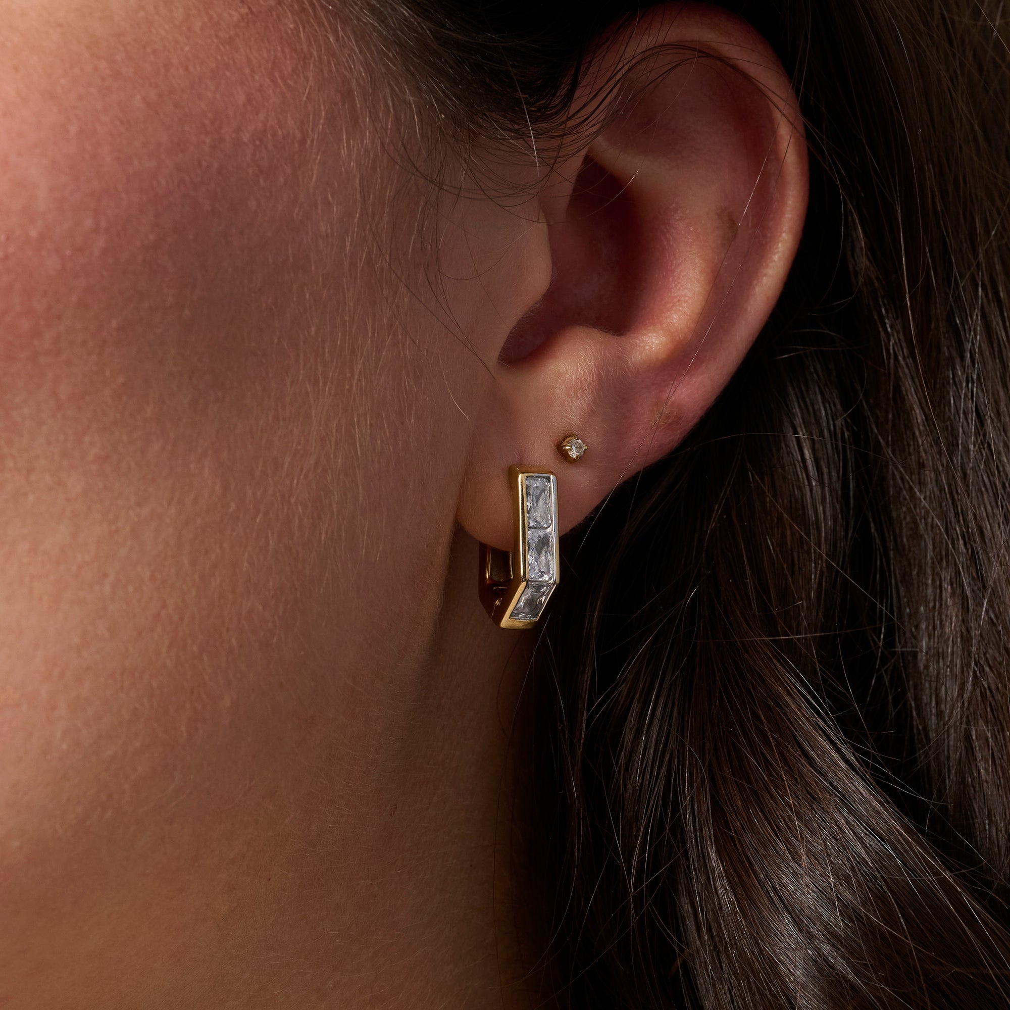 A close-up of a person's ear wearing a gold huggie hoop earring set with clear stones, alongside a small gold stud earring.

Gros plan sur l'oreille d'une personne portant une boucle d'oreille anneau dorée sertie de pierres transparentes, accompagnée d'une petite boucle d'oreille dorée.